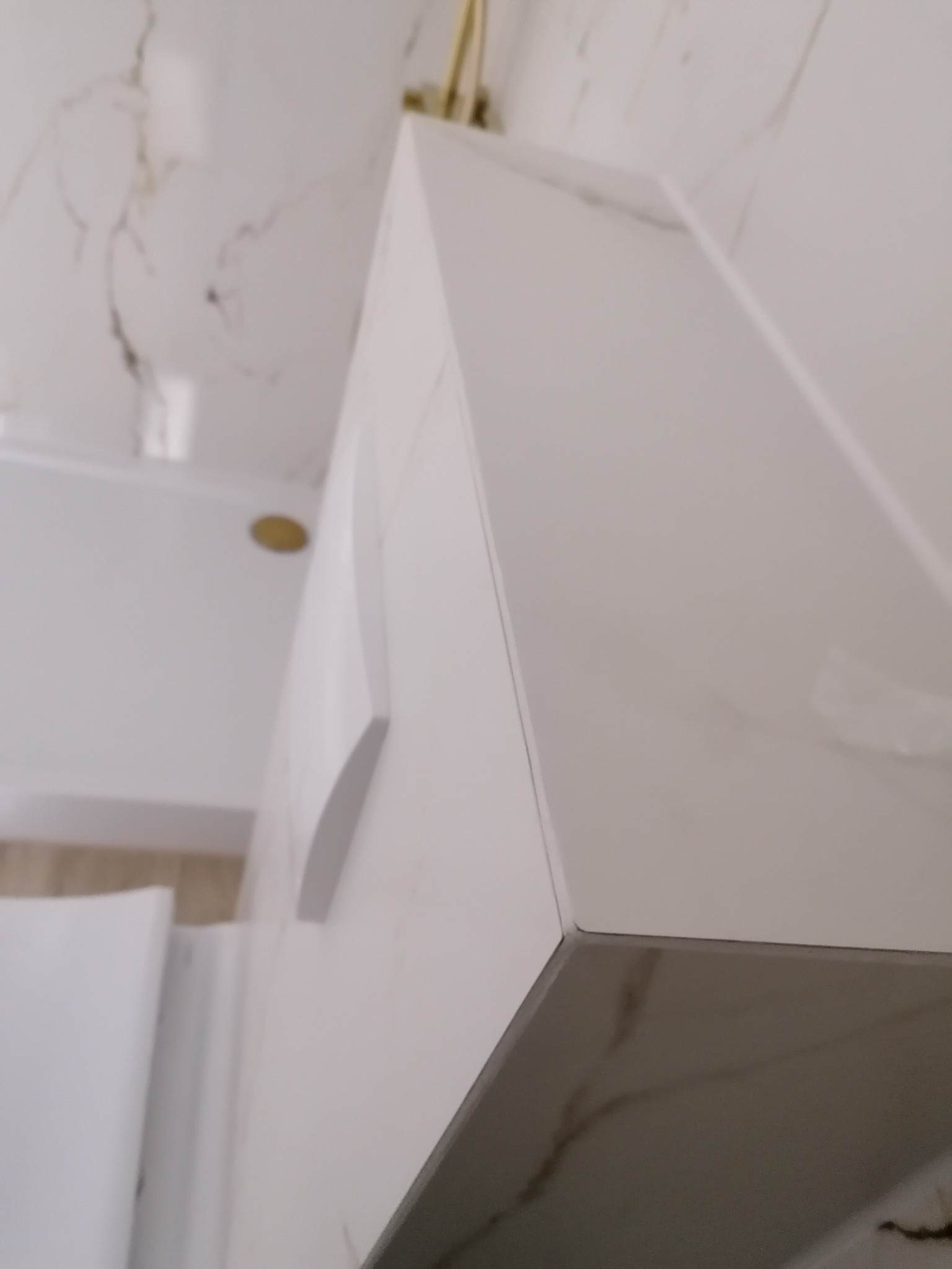 Wykończony narożnik zabudowy w łazience, płytki imitujące marmur z delikatnym wzorem, precyzyjne połączenie krawędzi, widoczny fragment armatury w kolorze złotym i elementu wanny.