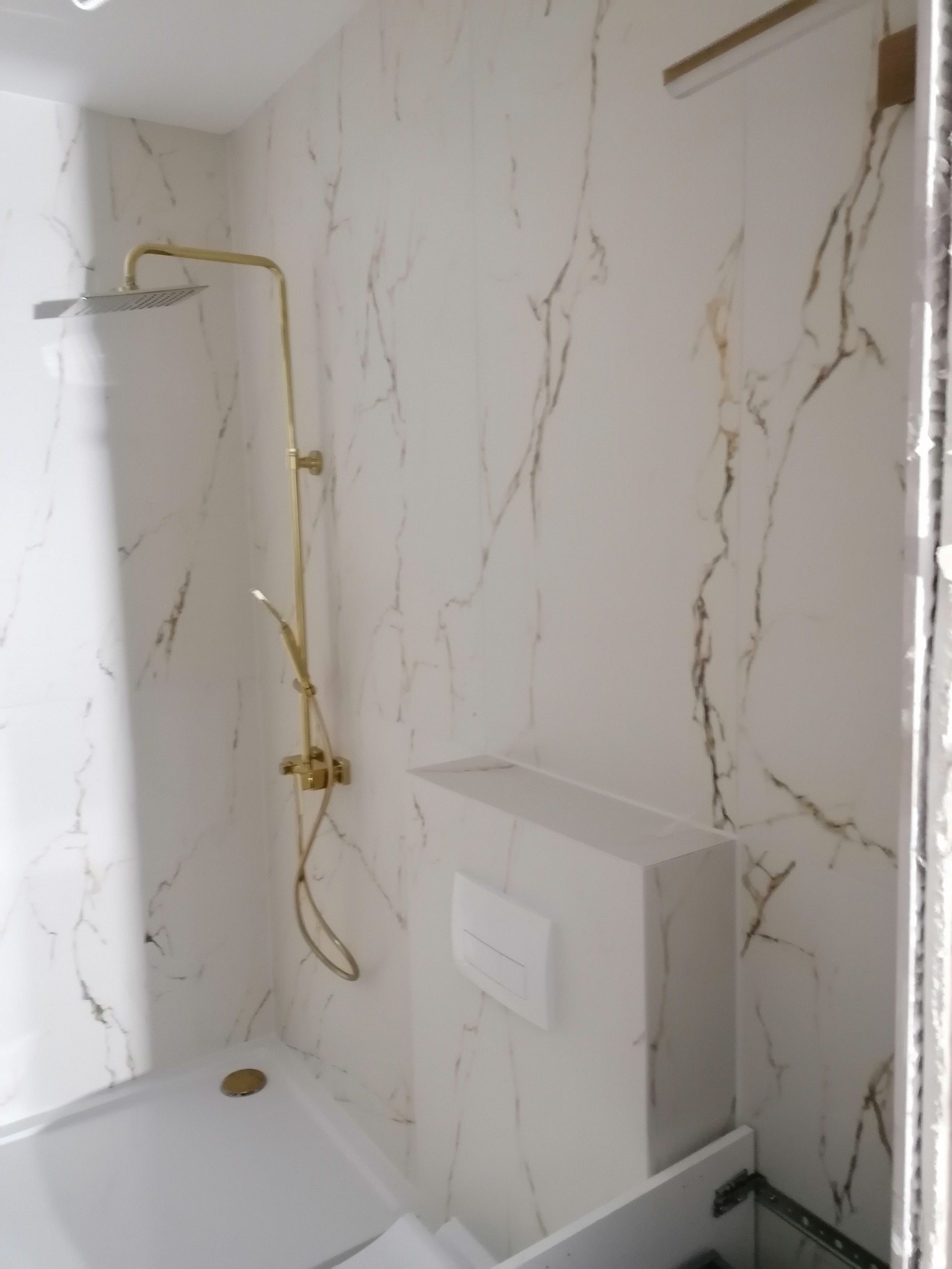 Wykończona łazienka z kabiną prysznicową i złotą armaturą na tle płytek imitujących marmur z wyraźnym wzorem żyłkowania.