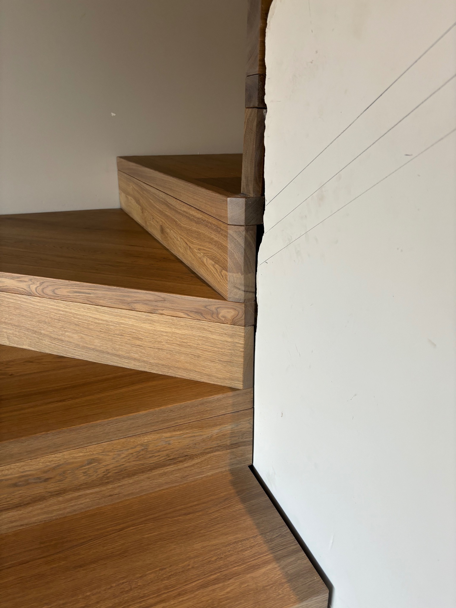 Fragment drewnianych schodów z widocznymi trzema stopniami, przy ścianie z zaznaczonymi liniami pomocniczymi.