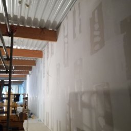 Sławomir Wajman - Cztery Kąty - Wnętrze w trakcie szpachlowania ścian, widoczny podnośnik nożycowy i sufit z blachy trapezowej.
