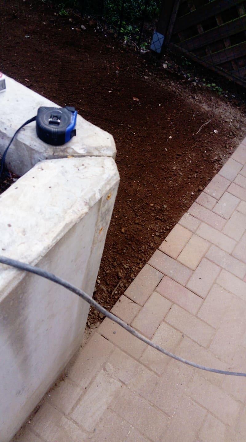 Przygotowanie podłoża pod kostkę brukową: wyrównana ziemia, ułożona kostka w jodełkę, betonowy obrzeże i zwinięta miarka.