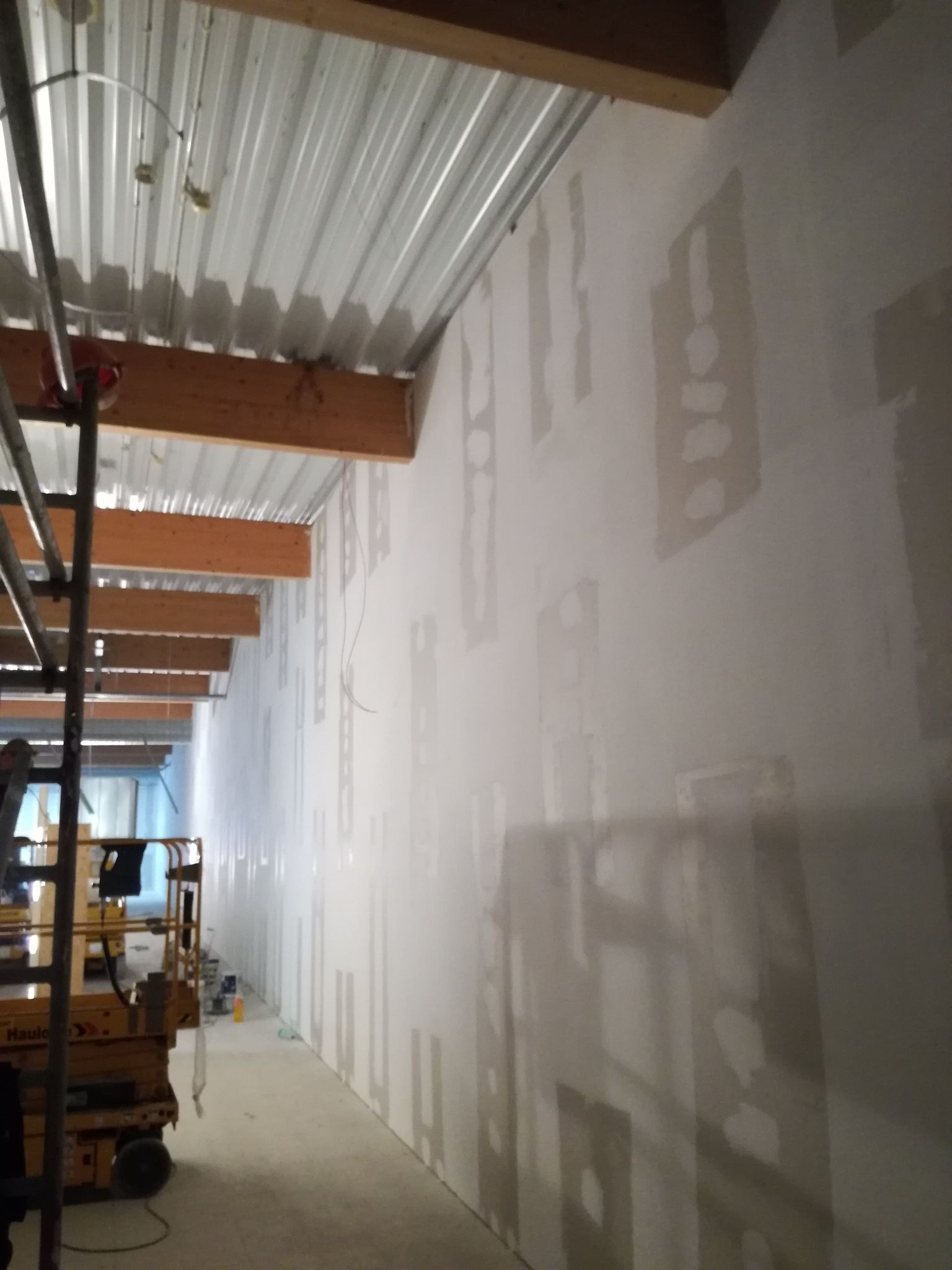Wnętrze w trakcie szpachlowania ścian, widoczny podnośnik nożycowy i sufit z blachy trapezowej.