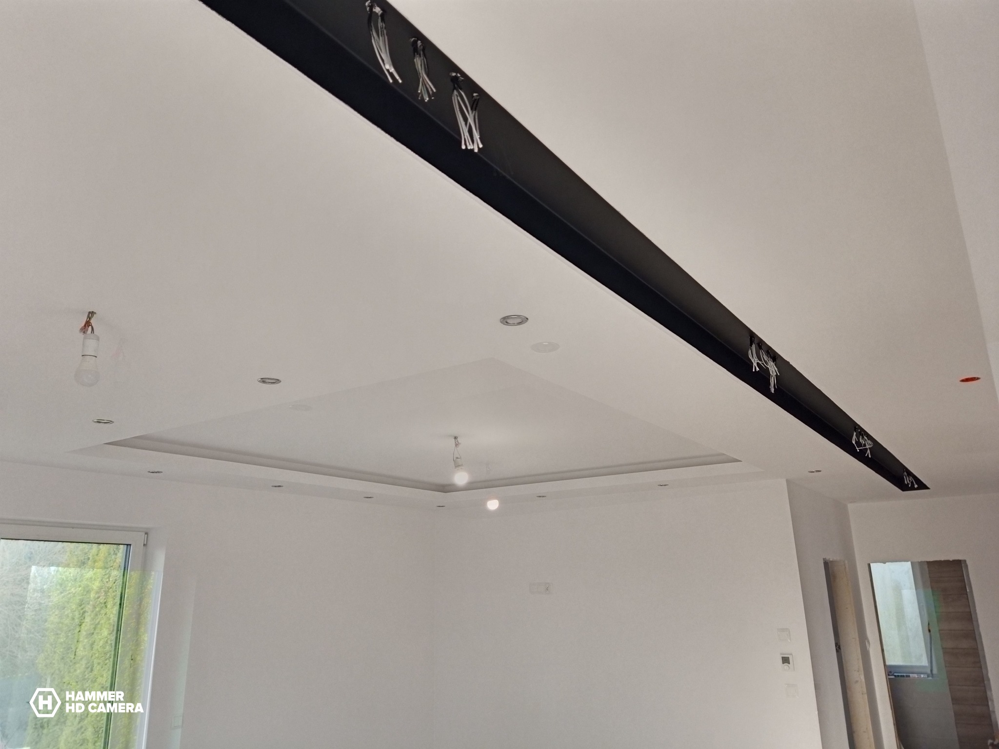 Nowoczesne wykończenie sufitu z czarną belką konstrukcyjną i oświetleniem punktowym, widoczne kable instalacji elektrycznej, wnętrze w trakcie remontu.