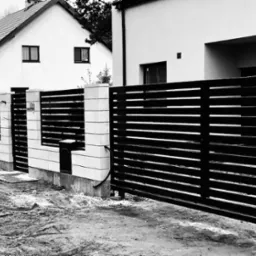 Nowoczesna brama wjazdowa z poziomymi, czarnymi panelami, osadzona w białych, murowanych słupkach, na tle dwóch domów i błotnistego podjazdu.