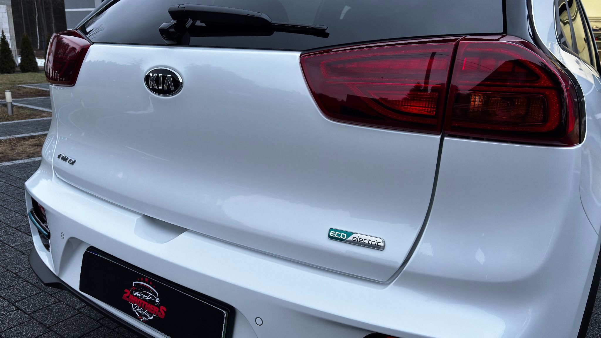 Tył białego samochodu Kia Niro Eco Electric po detailingu, widoczne logo firmy detailingowej na ramce tablicy rejestracyjnej.
