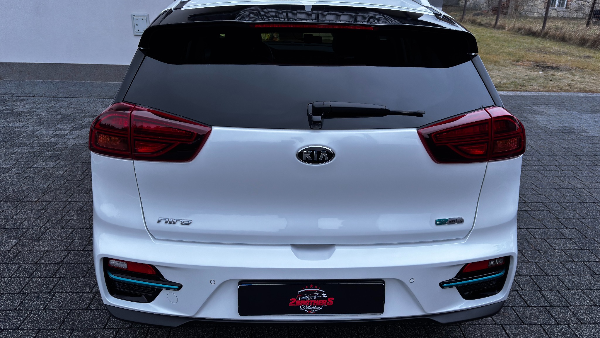 Tył białego samochodu Kia Niro EV po myciu, widoczne logo firmy detailingowej na tablicy rejestracyjnej.