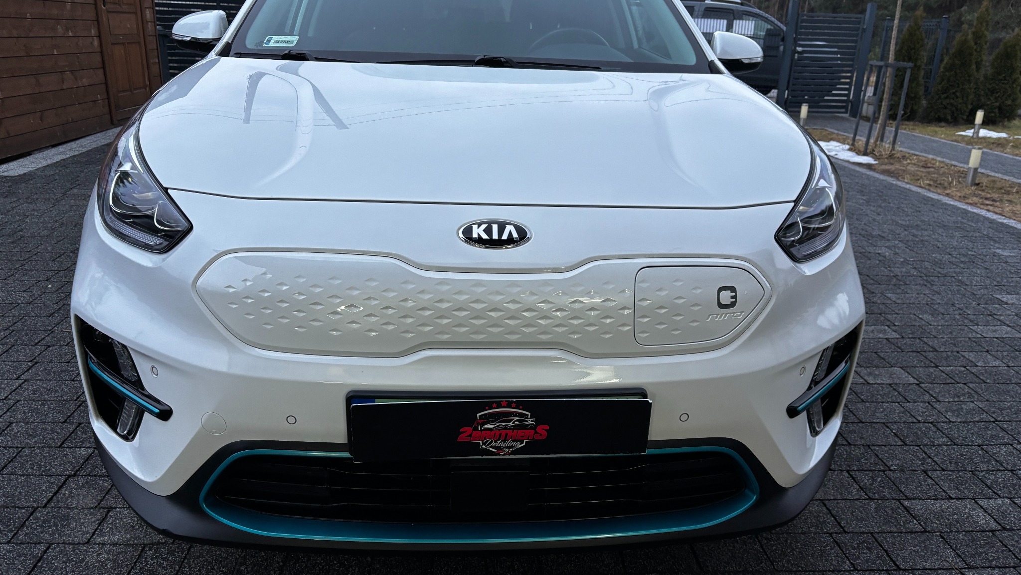 Przód białego samochodu Kia Niro EV z widocznym logo firmy detailingowej na tablicy rejestracyjnej.