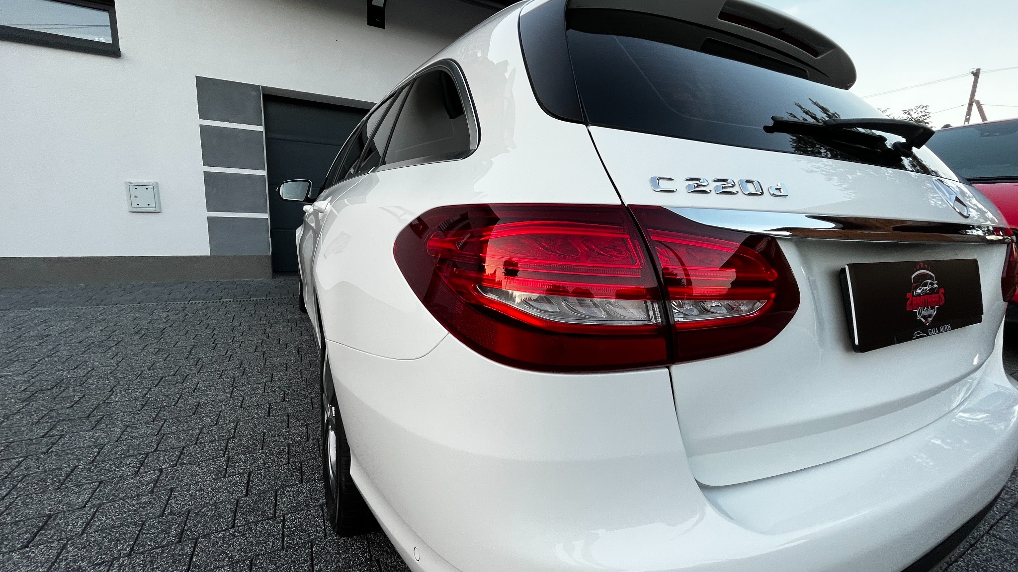 Tył białego kombi Mercedes-Benz C220d z widocznym logo firmy detailingowej na tablicy rejestracyjnej, zaparkowanego na kostce brukowej przed budynkiem.