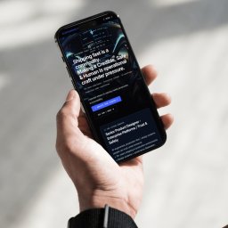 Edamame - Osoba trzyma smartfon z widoczną stroną internetową prezentującą projekt interfejsu użytkownika z tekstem o budowaniu zaufania i bezpieczeństwa w systemach AI.