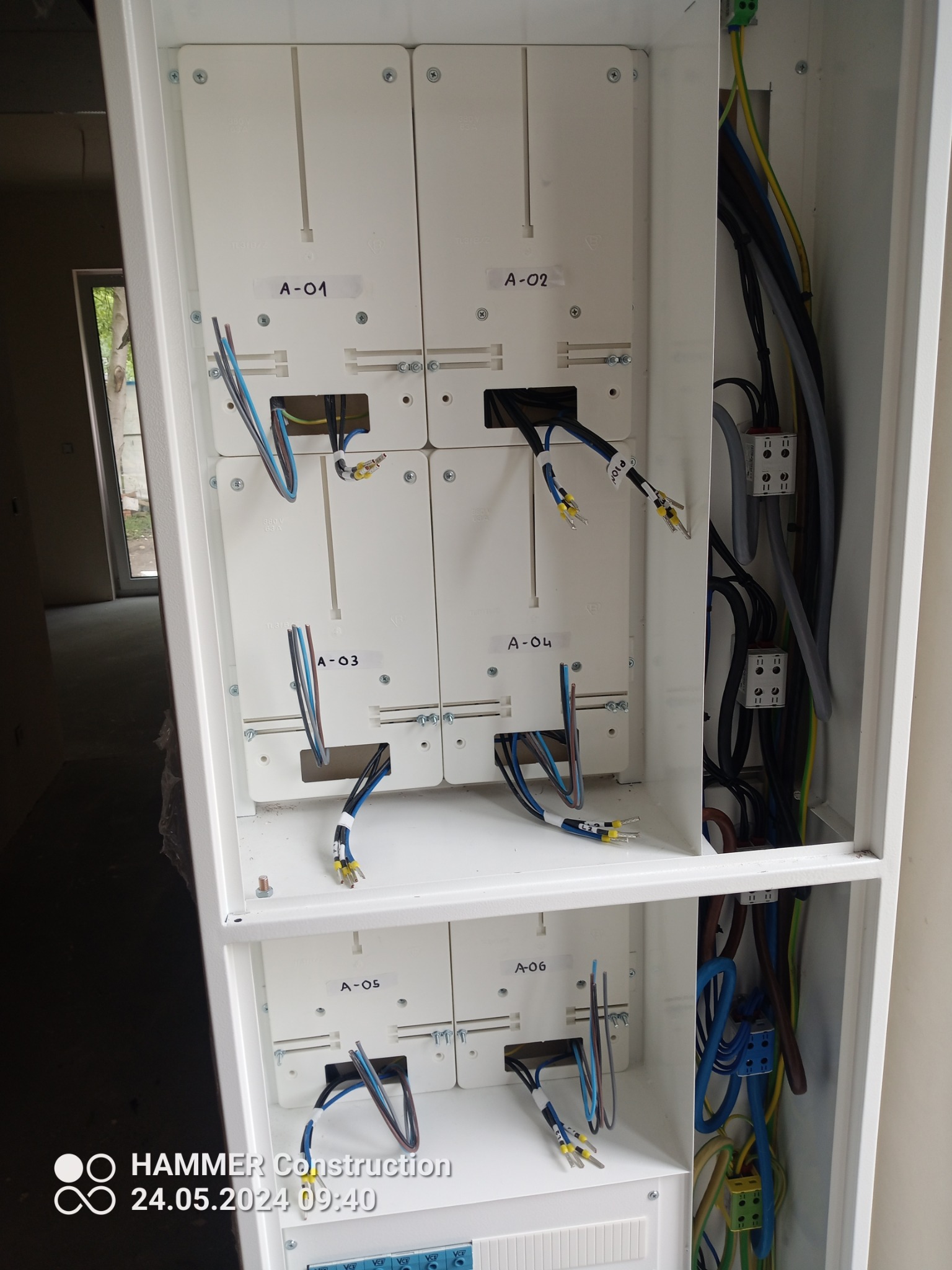 Otwarta skrzynka elektryczna z modułowymi elementami oznaczonymi A-01 do A-06, widoczne przewody z końcówkami tulejkowymi oraz inne kable wewnątrz skrzynki.