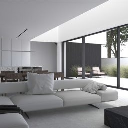 KAGIZE AND PARTNERS Dominik Kagize Ntibansiga - Minimalistyczny salon z białym narożnikiem, marmurowym stolikiem kawowym i widokiem na zewnętrzny taras z krzesłami i trawami ozdobnymi za dużym oknem.