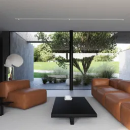 Minimalistyczny salon z brązową skórzaną sofą i fotelem, czarnym stolikiem kawowym z książkami, widokiem na ogród przez duże okno i nowoczesną lampą podłogową.
