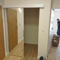 Krystian Rakoczy - Montaż przesuwnych drzwi lustrzanych w przedpokoju, widoczne narzędzia i części montażowe na podłodze.