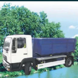 Biała ciężarówka z niebieskim kontenerem na tle zieleni i rzeki, widziana z boku, z logo Oferteo.pl w lewym górnym rogu.