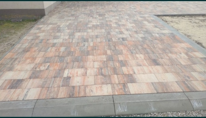 Ułożona nawierzchnia z prostokątnej kostki w odcieniach beżu i brązu, obrzeża wykończone szarym betonowym krawężnikiem.