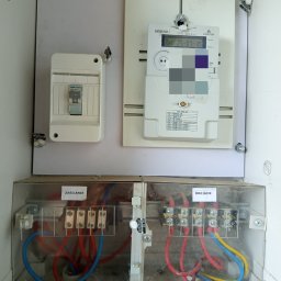 BLACKOUT Michał Uchman - Rozdzielnia elektryczna z licznikiem, bezpiecznikiem i okablowaniem. Widoczne oznaczenia 'Zasilanie' i 'Odejście'. Elementy zakurzone, co sugeruje długotrwałe użytkowanie.