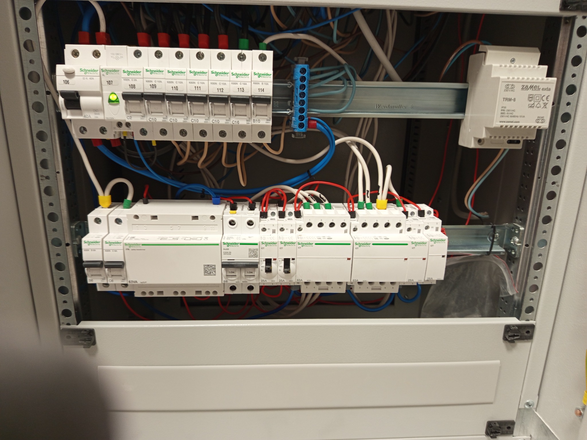 Rozdzielnica elektryczna z zamontowanymi bezpiecznikami i przewodami. Jeden z bezpieczników jest włączony, sygnalizując przepływ prądu. Widoczne elementy marki Schneider Electric.