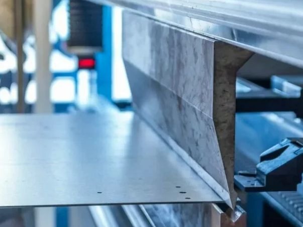 Proces gięcia blachy na prasie krawędziowej, widoczne narzędzia i obrabiany element w trakcie formowania.