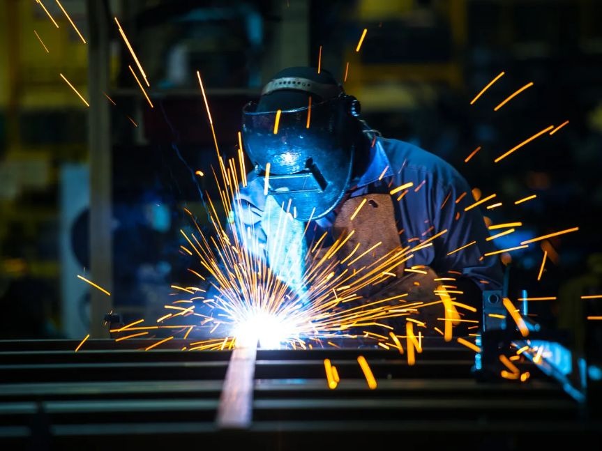 Spawanie metalu. Mężczyzna w masce spawalniczej łączy elementy stalowe, iskry rozbryzgują się na boki.