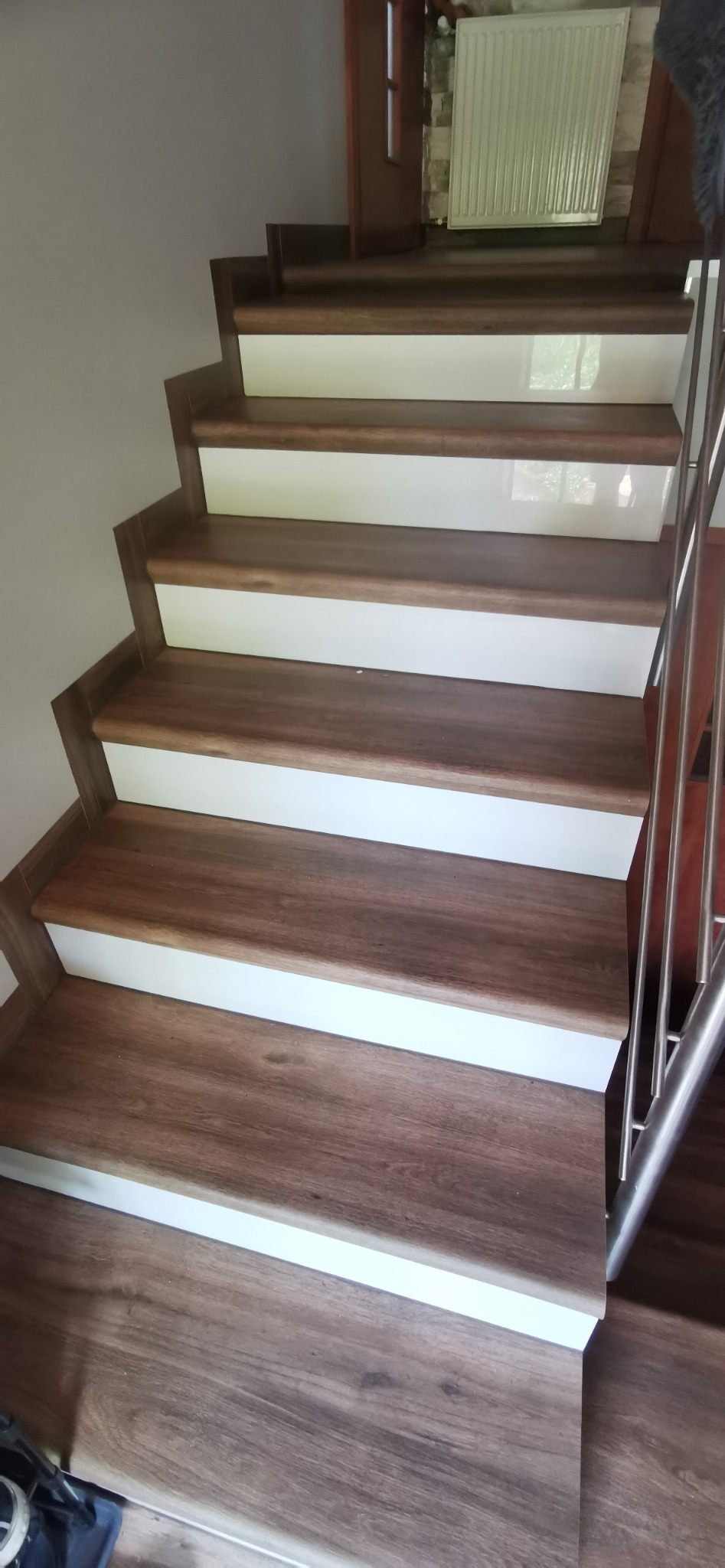 Schody wykończone panelami drewnopodobnymi z białymi podstopnicami i metalową barierką, widoczne z dołu.