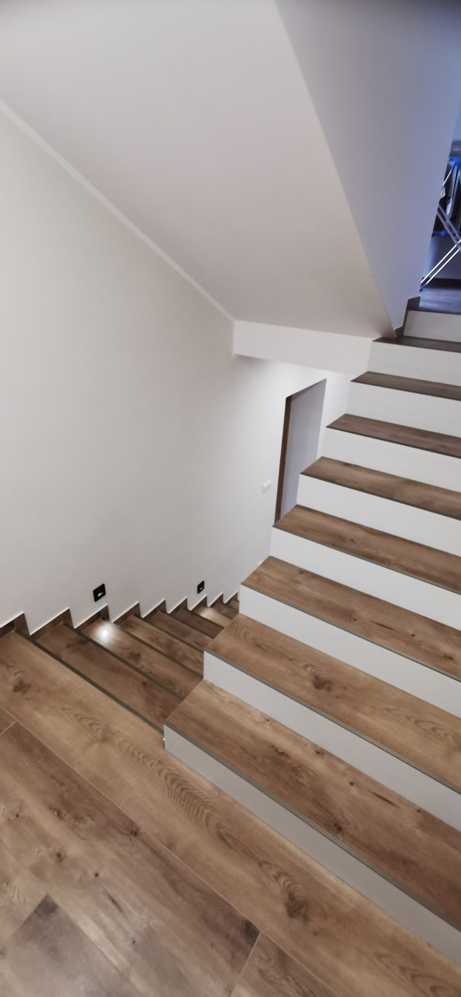 Nowoczesne schody z drewnopodobnymi panelami na stopniach i podświetleniem LED wzdłuż ściany, widok z góry.