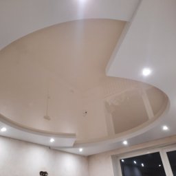 Satynpoland - Błyszczący sufit napinany w kształcie półkola z wbudowanymi punktowymi lampami LED, widok z dołu na tle surowych ścian przed wykończeniem.