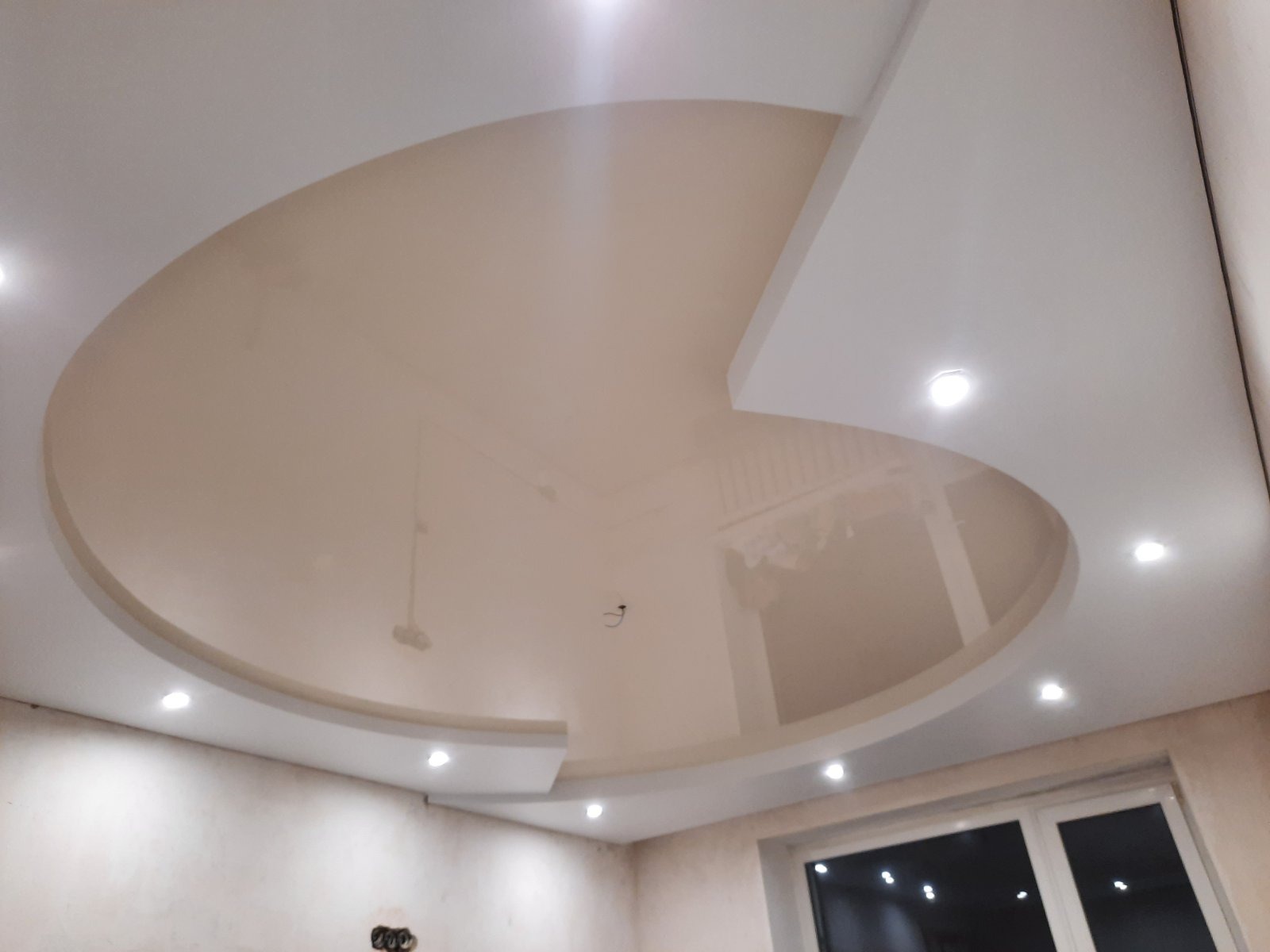 Błyszczący sufit napinany w kształcie półkola z wbudowanymi punktowymi lampami LED, widok z dołu na tle surowych ścian przed wykończeniem.