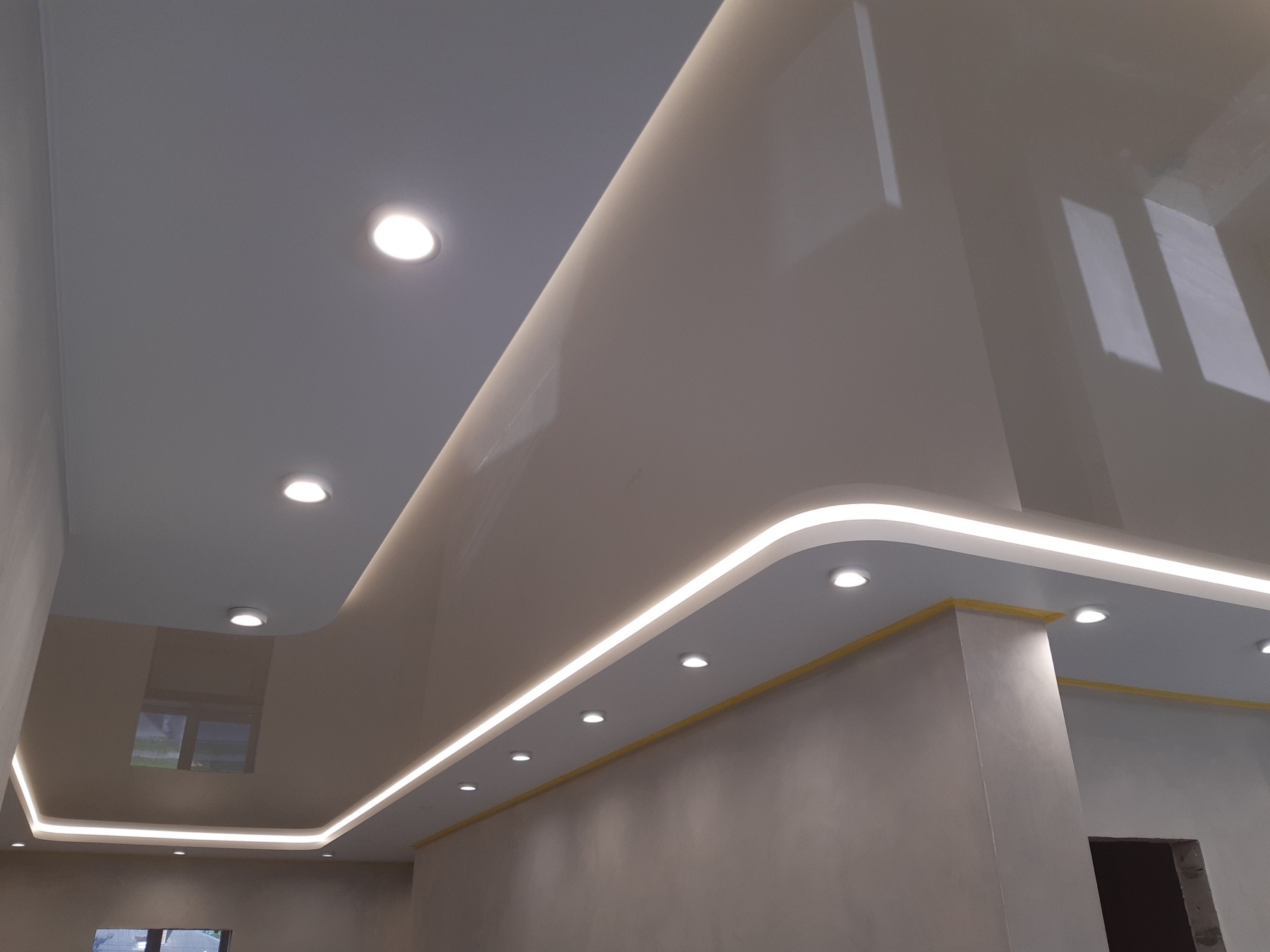 Błyszczący, dwupoziomowy sufit z wbudowanym oświetleniem LED i punktowymi lampami, widok z dołu.