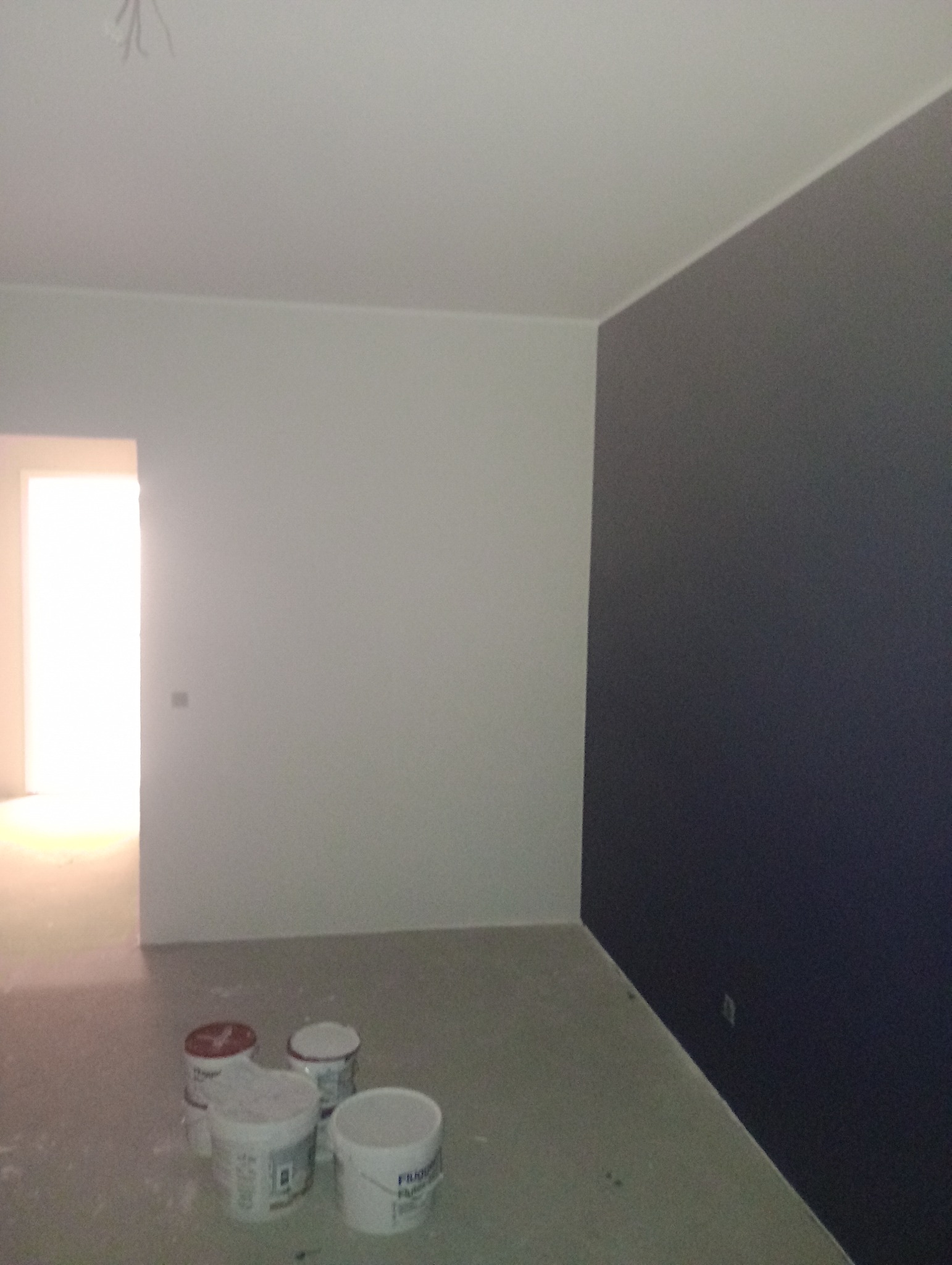 Świeżo pomalowane wnętrze w Kościerzynie, z jedną ścianą w kolorze ciemnego granatu, a resztą na biało. Na podłodze stoją puszki z farbą, widoczny otwarty pokój w tle.