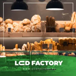 Półki piekarni wypełnione różnorodnym pieczywem: chleb pszenny, bagietki, bułki, oświetlone lampami sufitowymi, z logo firmy LED Factory na pierwszym planie.
