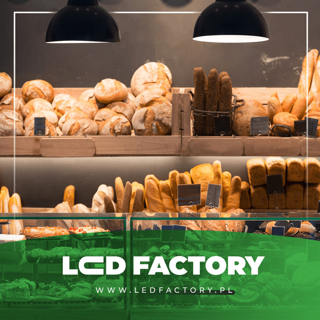 Półki piekarni wypełnione różnorodnym pieczywem: chleb pszenny, bagietki, bułki, oświetlone lampami sufitowymi, z logo firmy LED Factory na pierwszym planie.