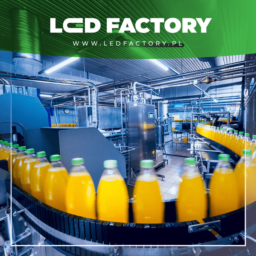 Linia produkcyjna z butelkami wypełnionymi żółtym napojem, widoczne rury i maszyny, w tle logo firmy LCD Factory.