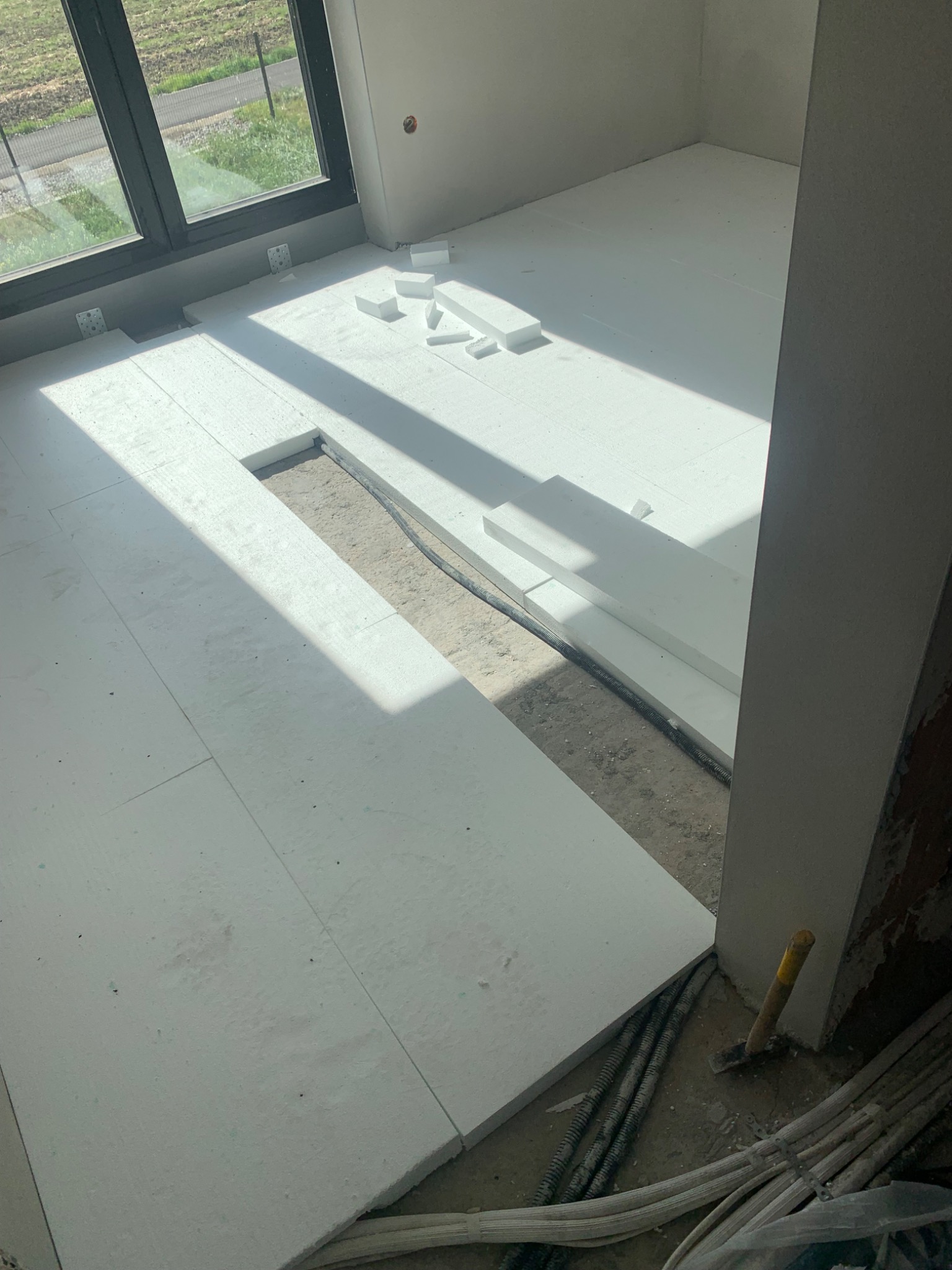 Podłoga w trakcie ocieplania styropianem, widoczne kable w peszlach i młotek przy ścianie.