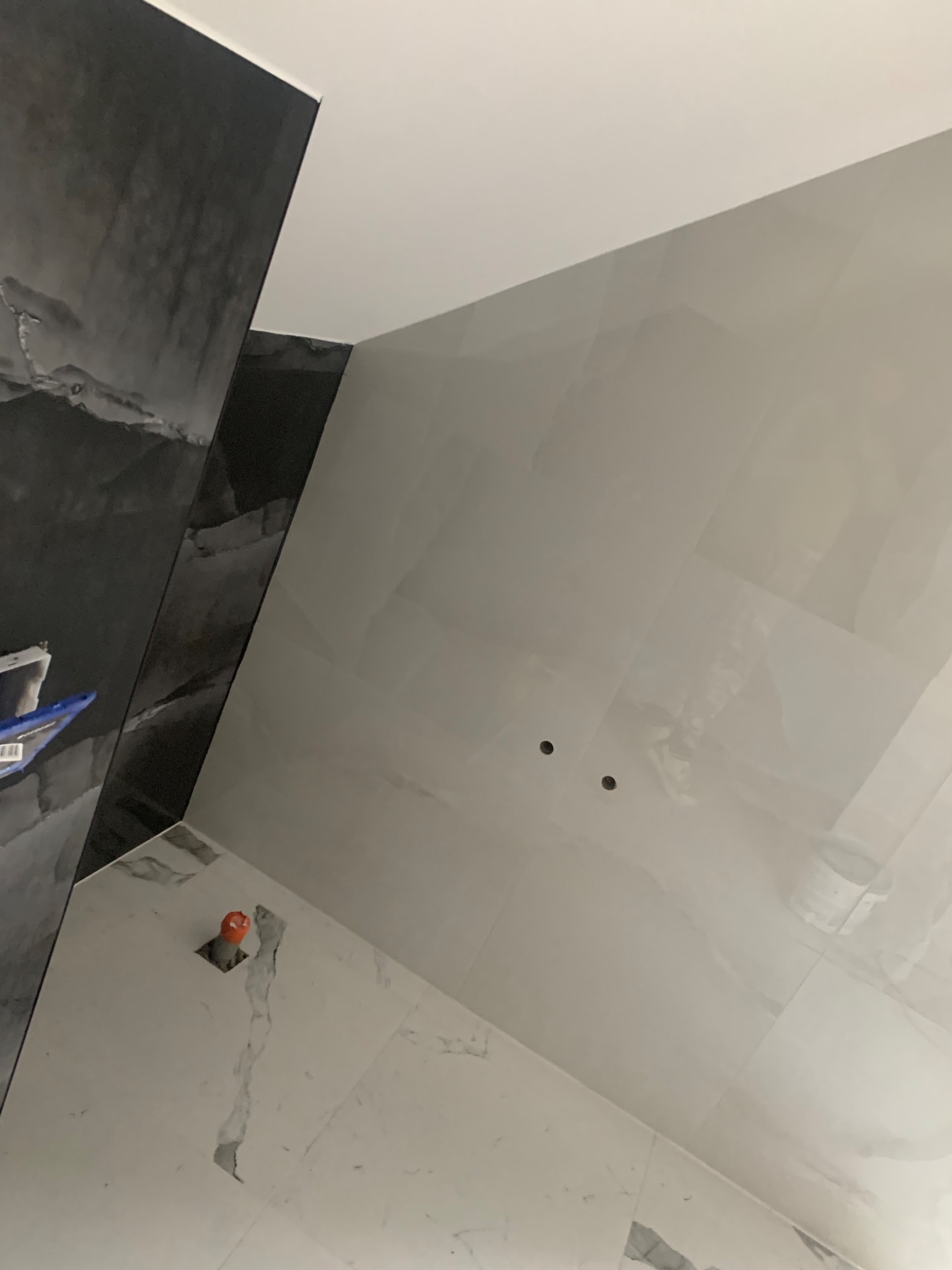 Ściany łazienki wyłożone jasnymi i ciemnymi płytkami imitującymi marmur, widoczne otwory na oświetlenie i fragment instalacji hydraulicznej w podłodze.