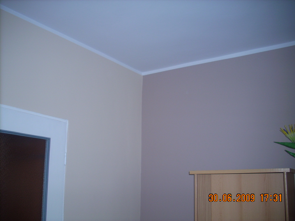 Pokój po malowaniu ścian na dwa kolory: beżowy i brązowy, z widoczną białą listwą przypodłogową i fragmentem mebla. Na zdjęciu widoczny datownik.