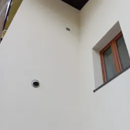 Jasna ściana po malowaniu z kratką wentylacyjną i oknem z brązową ramą. Widoczne rusztowanie z folią ochronną. Ciemny sufit w rogu.