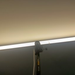 Bart-Dom - Gładki, jasny sufit równomiernie oświetlony podłużną lampą, z fragmentem statywu roboczego widocznym w dolnej części kadru.