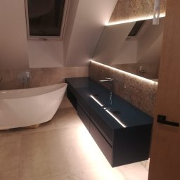 Bart-Dom - Nowoczesna łazienka na poddaszu z białą wanną wolnostojącą, ciemnoniebieską szafką podwójną z umywalkami i lustrem z podświetleniem LED. Jasne płytki i okno dachowe.