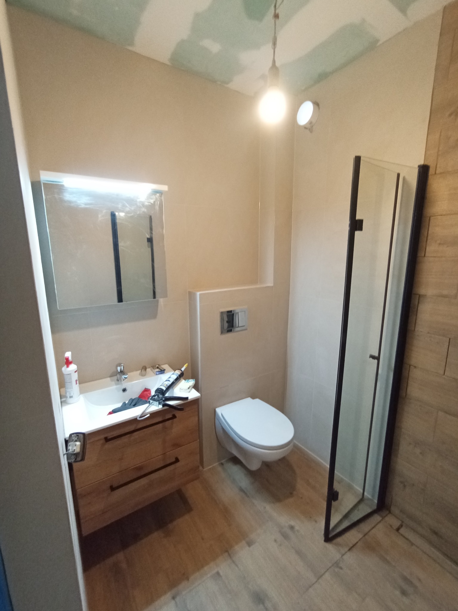 Montaż kabiny prysznicowej i umywalki w łazience w trakcie remontu. Widoczne narzędzia i materiały budowlane. Sufit z płyt kartonowo-gipsowych.