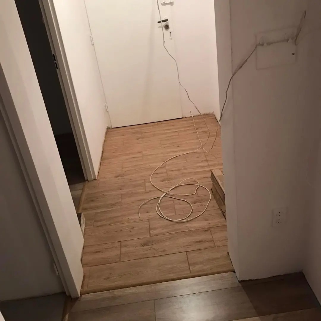 Korytarz z nowo ułożoną podłogą z paneli imitujących drewno, widoczne kable i listwy przypodłogowe w trakcie montażu.