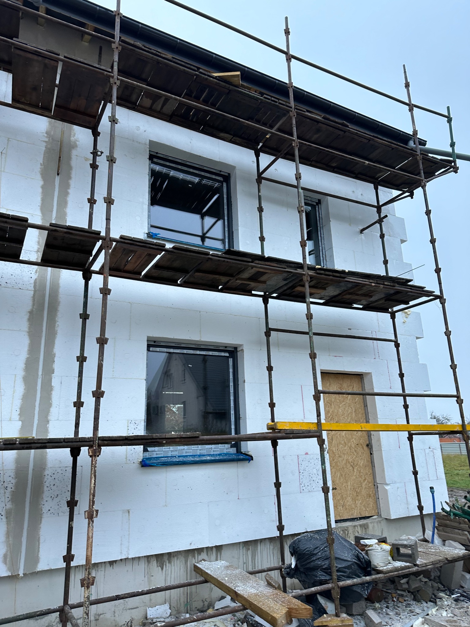 Budynek w trakcie ocieplania, widoczne rusztowanie, styropianowe bloki elewacyjne i okna z folią ochronną.