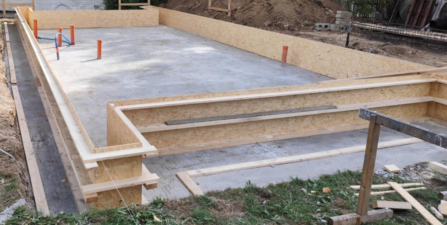 Fundament płyta z izolacją i instalacją kanalizacyjną, szalunek z płyty OSB. Widok na betonową płytę fundamentową w trakcie budowy domu.