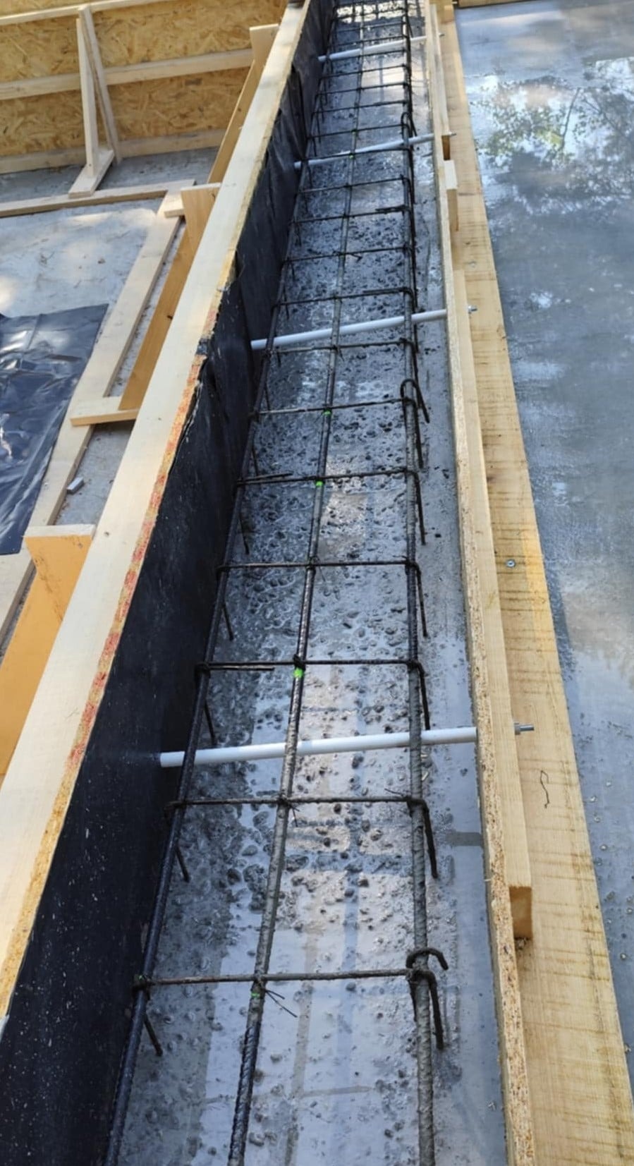 Zbrojenie fundamentu w szalunku, widoczne pręty i beton. Realizacja w Żurowej. Detal konstrukcji przed zalaniem.