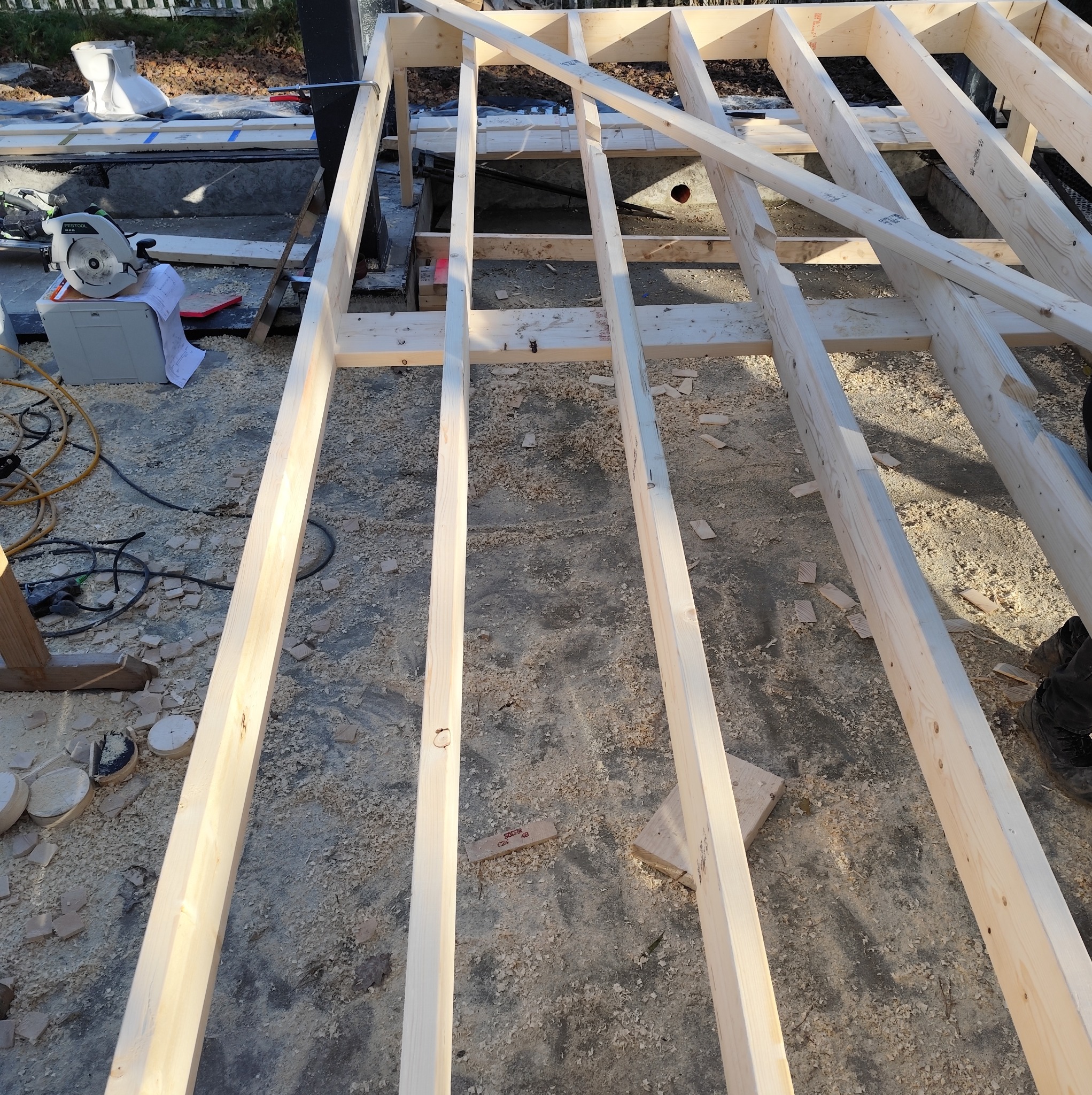 Konstrukcja podłogi z belek drewnianych w trakcie budowy domu szkieletowego. Widoczne narzędzia i elementy konstrukcyjne.