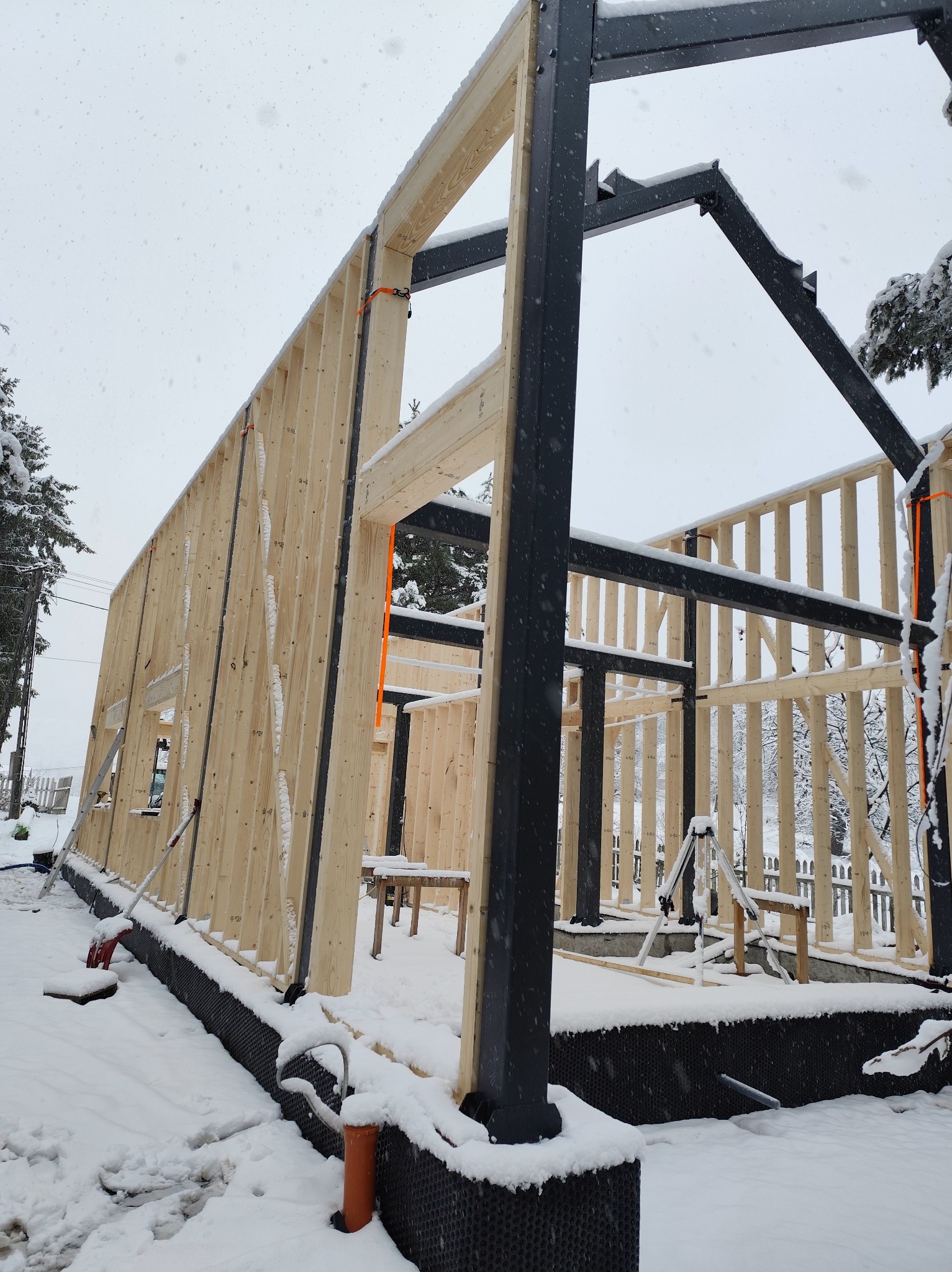 Konstrukcja domu szkieletowego w Żurowej, w trakcie budowy. Widoczne drewniane elementy ścian i stalowe słupy. Śnieg na zewnątrz.