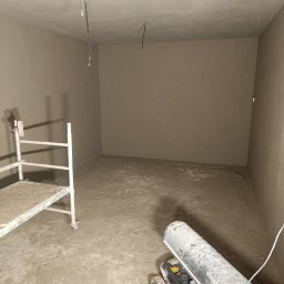 DAW-TYNK - Wnętrze pomieszczenia po świeżo wykonanych pracach wykończeniowych, widoczny agregat grzewczy Duraterm, pozostałości materiału na podłodze i rusztowaniu.
