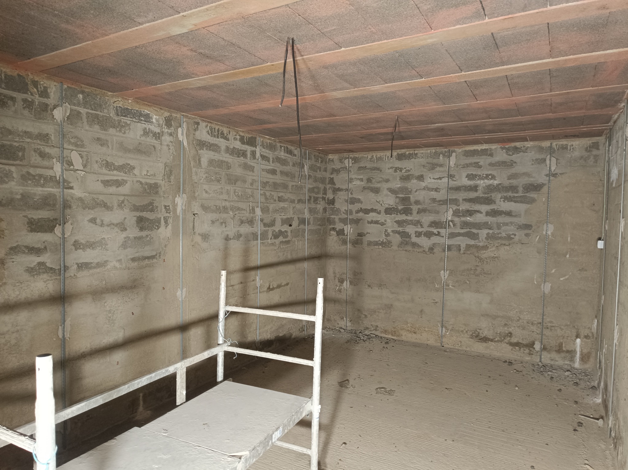 Surowe ściany z betonu komórkowego z widocznymi metalowymi listwami pionowymi, przygotowane do prac wykończeniowych, z rozstawionym rusztowaniem malarskim i widoczną instalacją elektryczną...