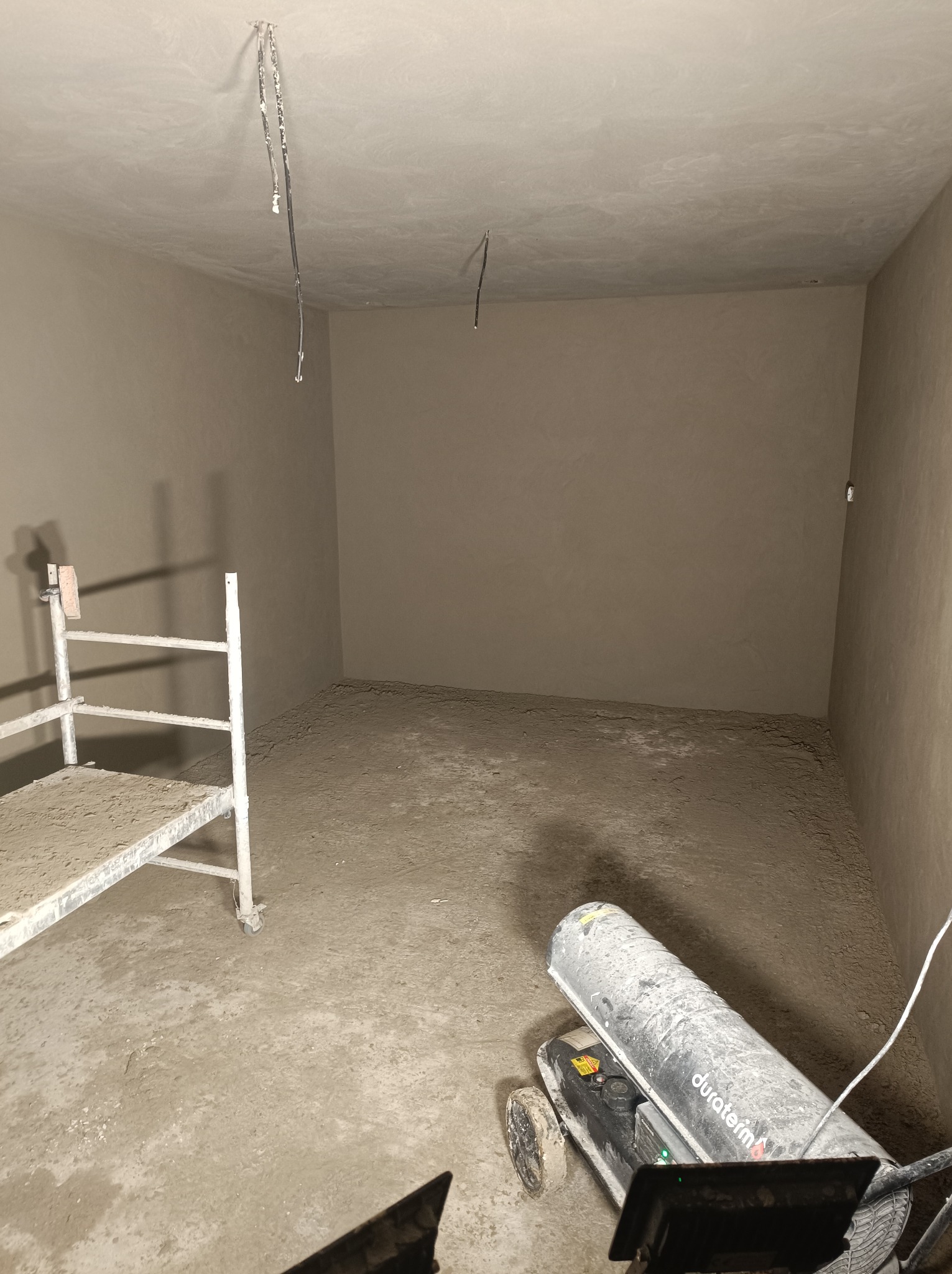 Wnętrze pomieszczenia po świeżo wykonanych pracach wykończeniowych, widoczny agregat grzewczy Duraterm, pozostałości materiału na podłodze i rusztowaniu.