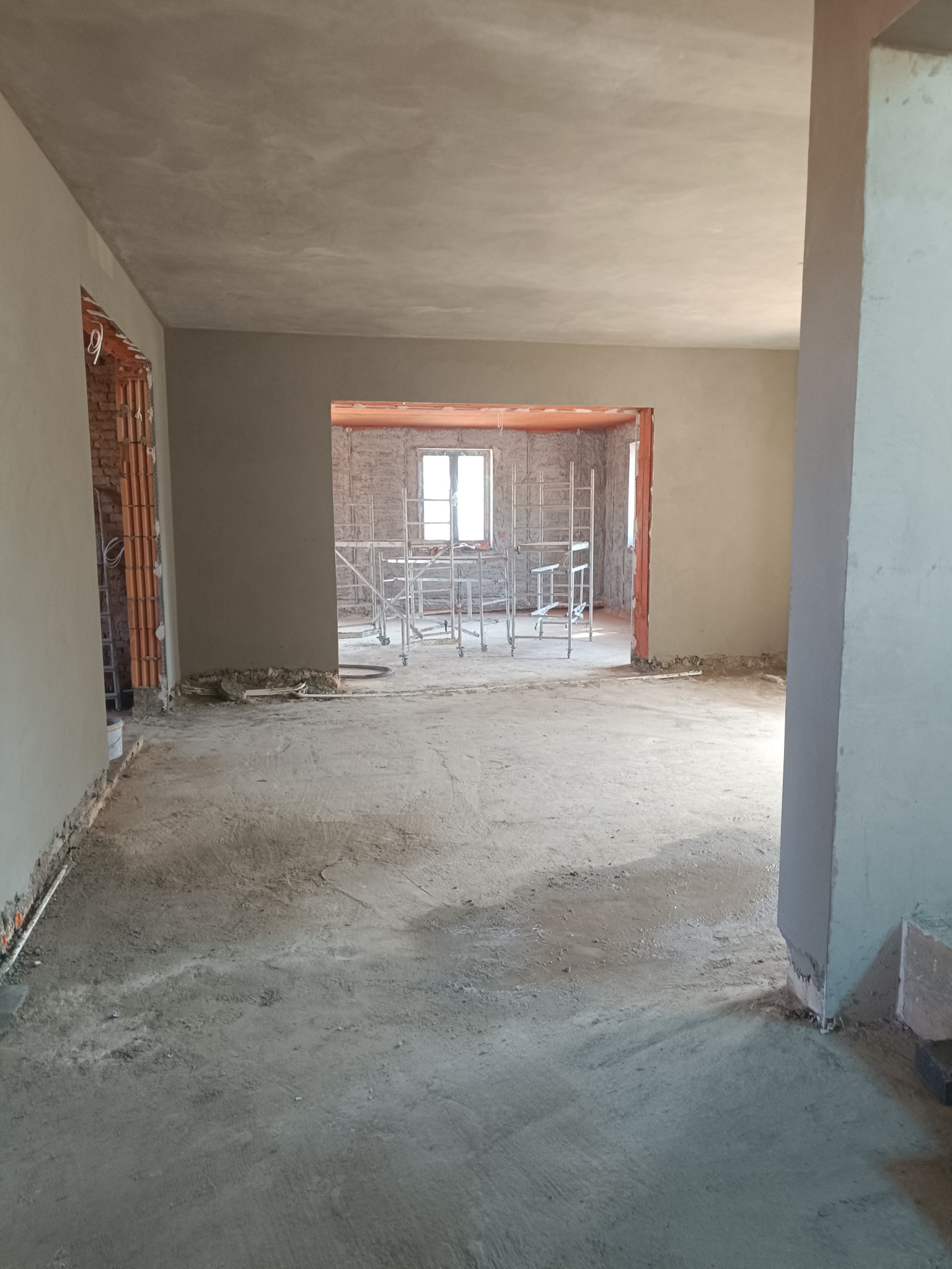 Surowe wnętrze po tynkowaniu ścian i sufitów, widoczne rusztowania w przejściach. Szara kolorystyka. Wnętrze w trakcie wykańczania, brak podłóg.