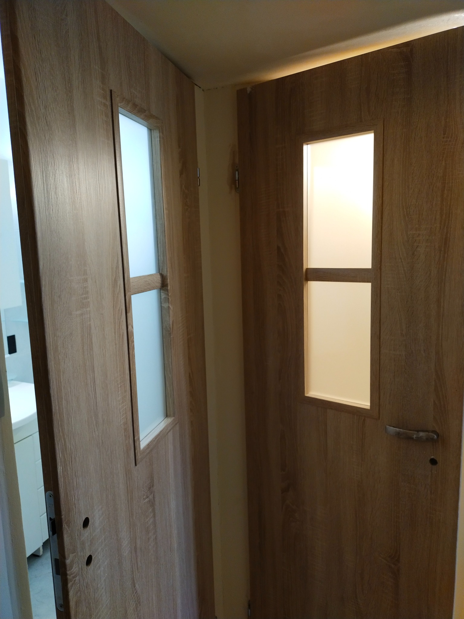 Dwa skrzydła drzwi wewnętrznych z panelami z mlecznego szkła, zamontowane w mieszkaniu w Łodzi, widoczne z perspektywy wnętrza pomieszczenia.